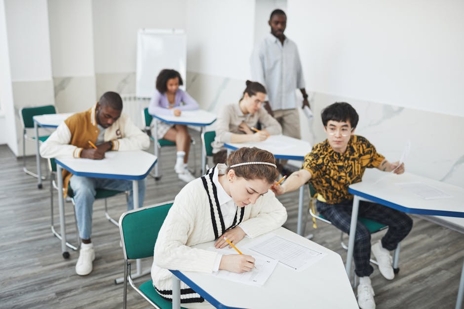 Group of students taking a test in a modern college classroom under teacher supervision